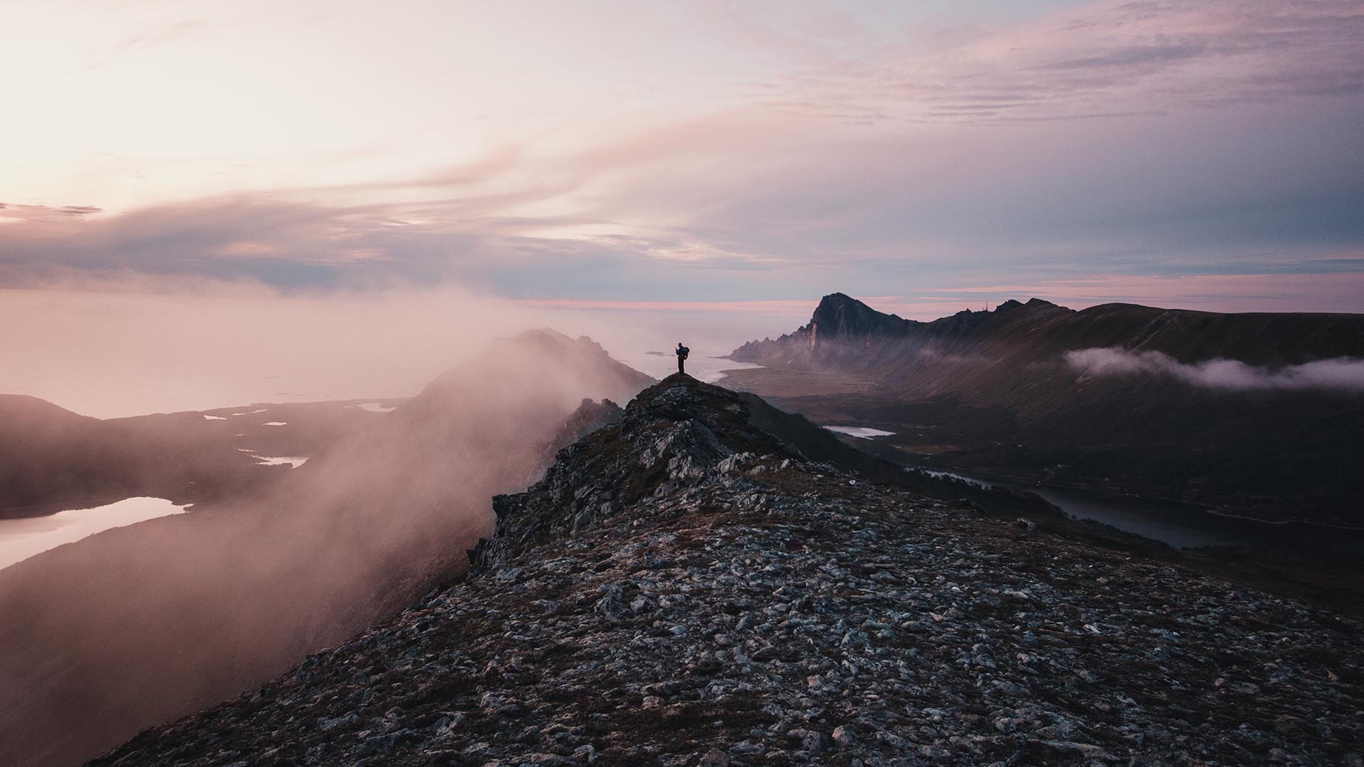 Mann auf Bergspitze mit Meer und Nebel im Hintergrund
