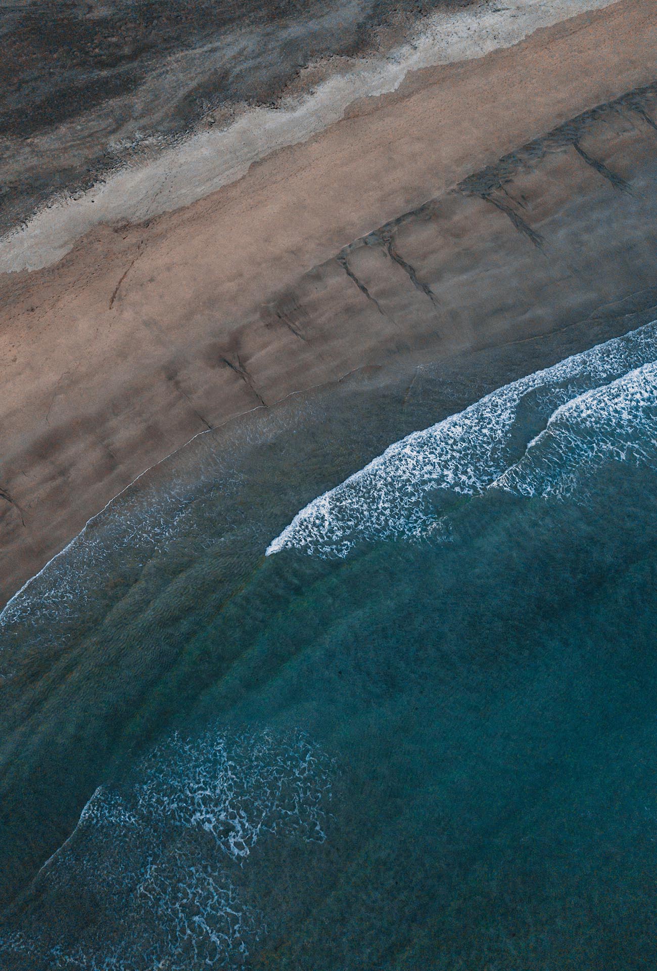 Luftbild von einem Strand, mit weißen Schaumkronen auf den Wellen.
